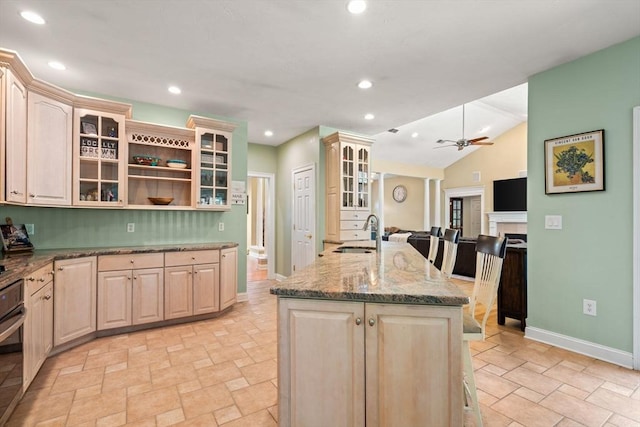 kitchen featuring a kitchen island with sink, light brown cabinetry, baseboards, open floor plan, and a sink