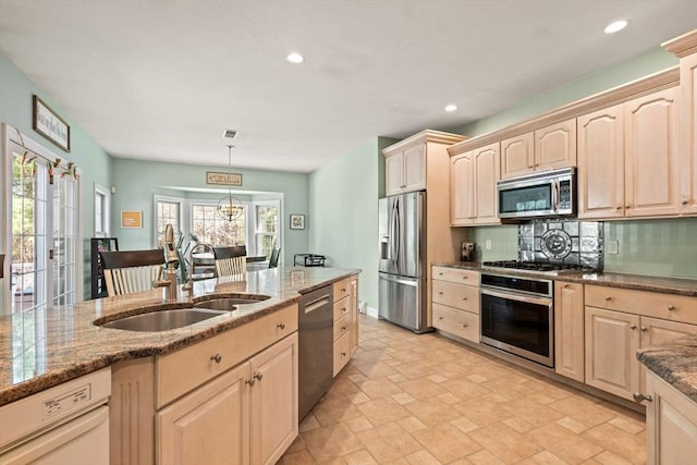 kitchen featuring a sink, dark stone countertops, appliances with stainless steel finishes, and light brown cabinetry