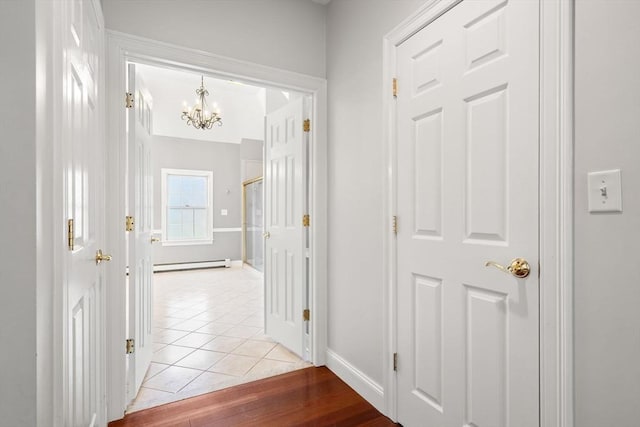 corridor featuring baseboards, a baseboard radiator, light tile patterned flooring, and a notable chandelier