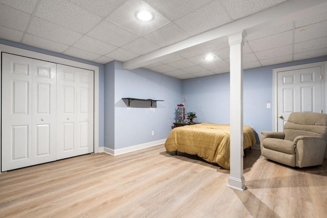 bedroom with baseboards, a paneled ceiling, wood finished floors, and a closet
