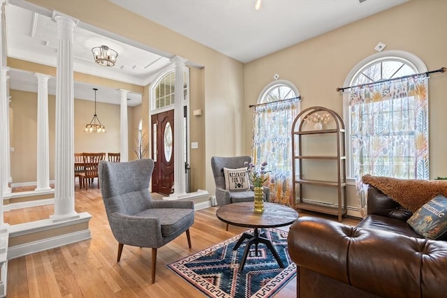 living area with ornate columns, a notable chandelier, and wood finished floors