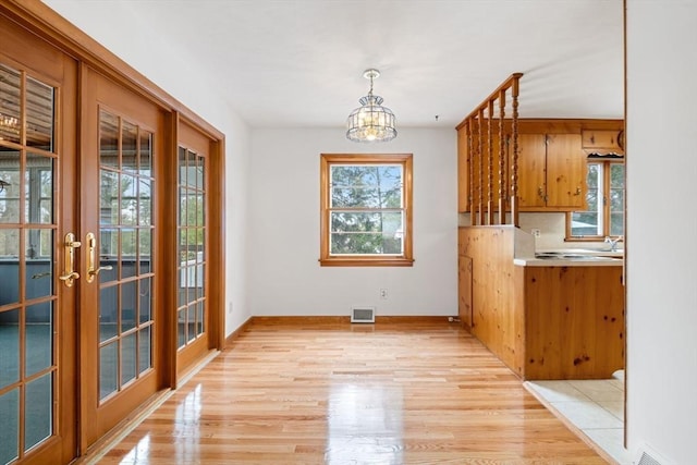 unfurnished dining area with light wood-type flooring, baseboards, visible vents, a notable chandelier, and french doors