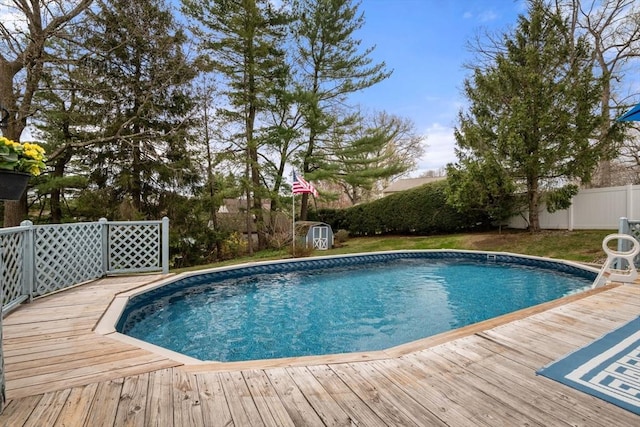 outdoor pool featuring an outdoor structure, a wooden deck, a fenced backyard, and a storage shed