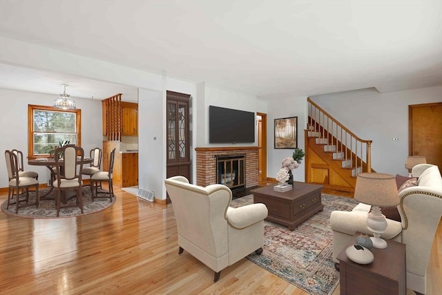 living area with an inviting chandelier, stairs, light wood-style floors, a fireplace, and visible vents