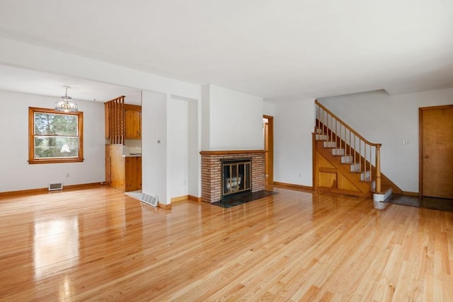 unfurnished living room featuring an inviting chandelier, stairs, light wood-style flooring, baseboards, and visible vents