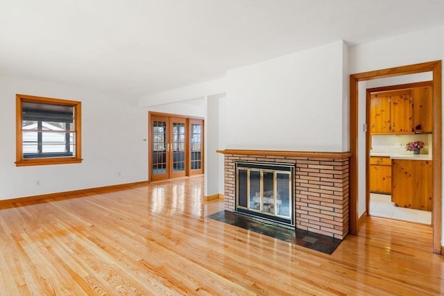 unfurnished living room with a fireplace, baseboards, french doors, and light wood-type flooring