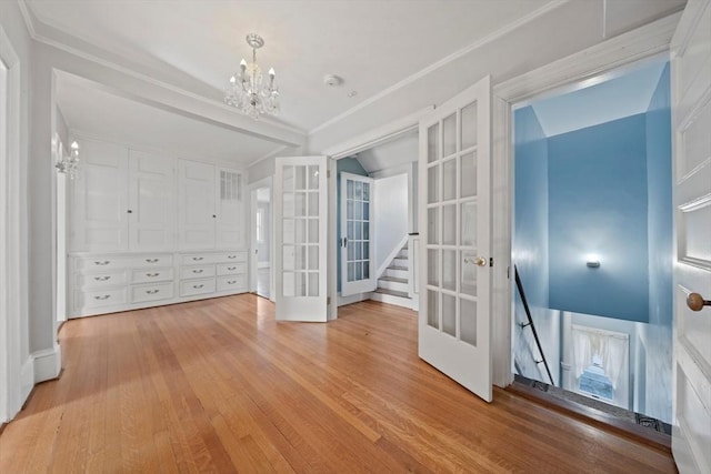 spare room featuring light wood finished floors, a chandelier, french doors, and crown molding