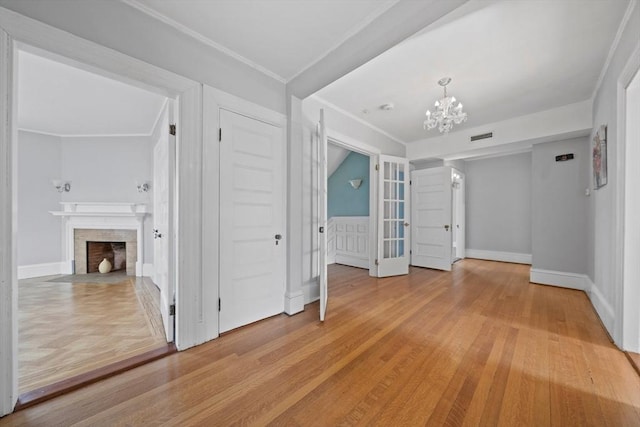 spare room with light wood-type flooring, an inviting chandelier, a fireplace, and visible vents