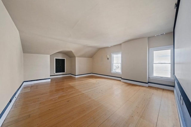 additional living space featuring vaulted ceiling, light wood-style floors, visible vents, and a wealth of natural light