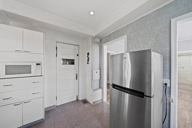 kitchen featuring white microwave, baseboards, granite finish floor, freestanding refrigerator, and white cabinets