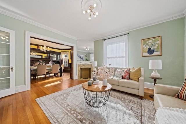 living area with a fireplace with flush hearth, hardwood / wood-style floors, crown molding, baseboards, and a chandelier