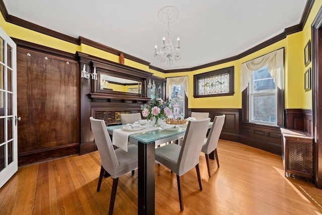 dining space with a chandelier, wainscoting, light wood-type flooring, and ornamental molding