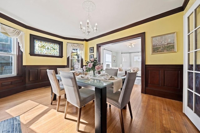 dining space featuring an inviting chandelier, light wood-style flooring, crown molding, and a wainscoted wall