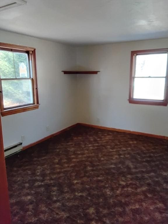 empty room with plenty of natural light, dark carpet, baseboard heating, and baseboards