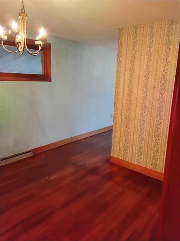 unfurnished room with baseboard heating, an inviting chandelier, wood finished floors, and baseboards