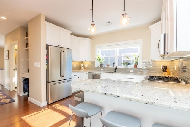 kitchen featuring backsplash, appliances with stainless steel finishes, a peninsula, white cabinetry, and a sink