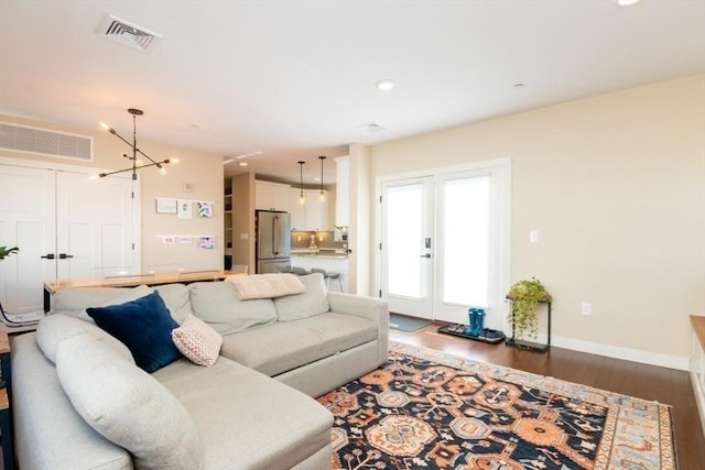 living area with visible vents, baseboards, a notable chandelier, and wood finished floors