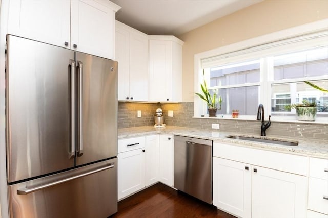 kitchen with a sink, backsplash, stainless steel appliances, white cabinets, and light stone countertops