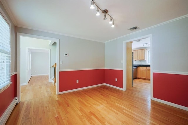 spare room with a baseboard heating unit, light wood finished floors, baseboards, and crown molding