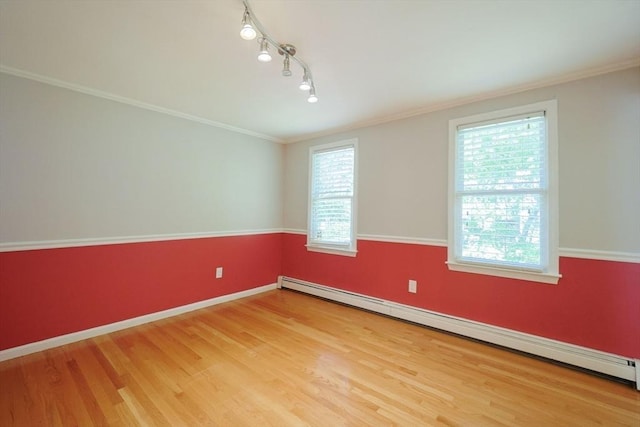 empty room featuring a baseboard heating unit, wood finished floors, ornamental molding, baseboards, and track lighting