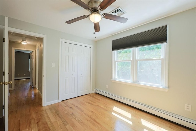 unfurnished bedroom with attic access, a baseboard heating unit, light wood-style flooring, a closet, and baseboards