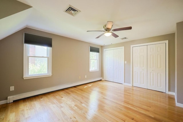 unfurnished bedroom featuring a baseboard heating unit, two closets, wood finished floors, baseboards, and lofted ceiling