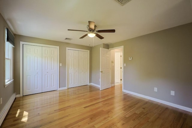 unfurnished bedroom with baseboard heating, multiple closets, light wood-style floors, and baseboards