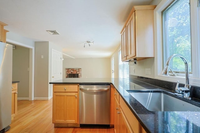 kitchen featuring stainless steel dishwasher, a sink, freestanding refrigerator, a peninsula, and healthy amount of natural light