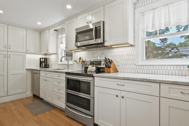 101 Eastern Ave, Woburn, MA 01801 - kitchen with stainless steel appliances, decorative backsplash, white cabinetry, light wood-style flooring, and recessed lighting