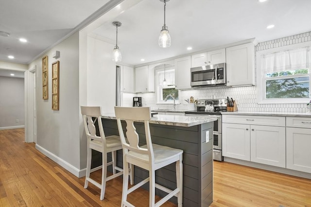 101 Eastern Ave, Woburn, MA 01801 - kitchen featuring appliances with stainless steel finishes, backsplash, a breakfast bar, light wood finished floors, and white cabinetry