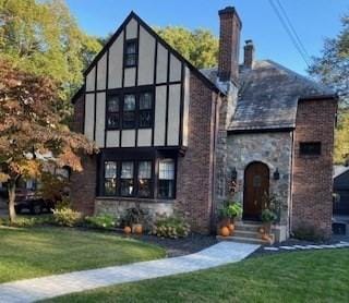 tudor house with entry steps, stone siding, a chimney, and a front lawn