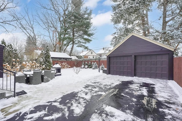 yard layered in snow featuring an outbuilding, outdoor dining area, a detached garage, and fence