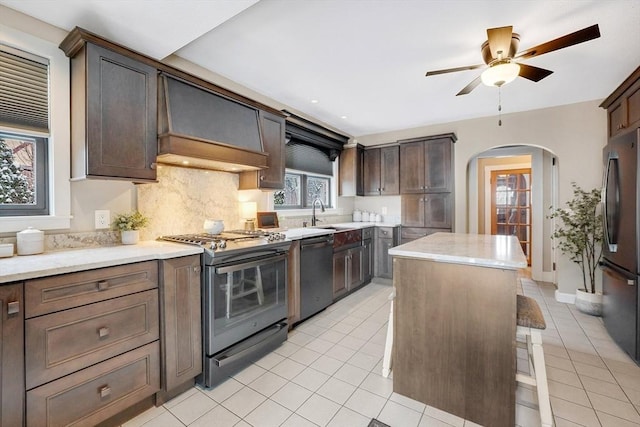 kitchen featuring arched walkways, light tile patterned flooring, stainless steel appliances, a sink, and a center island