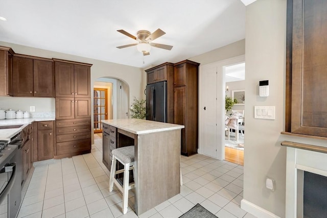 kitchen with arched walkways, light tile patterned flooring, a kitchen island, a ceiling fan, and black fridge