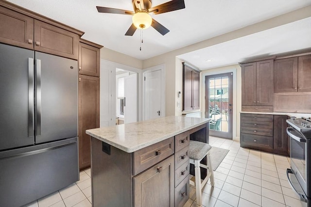 kitchen with range with gas stovetop, light stone counters, light tile patterned floors, freestanding refrigerator, and a kitchen breakfast bar