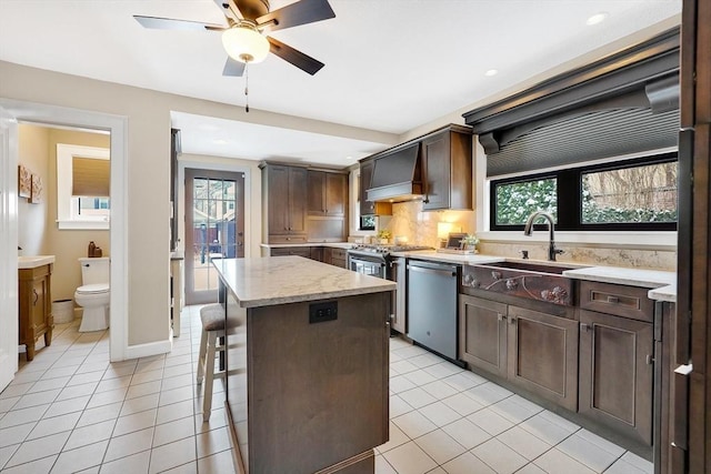 kitchen with appliances with stainless steel finishes, a center island, custom exhaust hood, a sink, and light tile patterned flooring