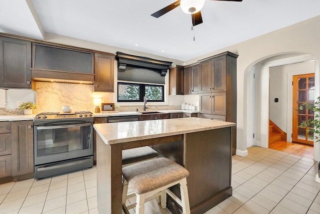 kitchen with stainless steel gas range, light tile patterned flooring, a sink, and tasteful backsplash