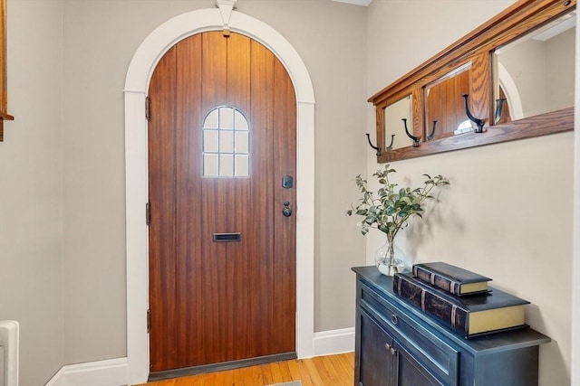 foyer entrance with light wood-type flooring, baseboards, and arched walkways