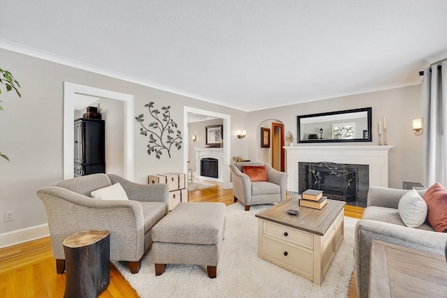 living area featuring arched walkways, light wood finished floors, a fireplace, and baseboards