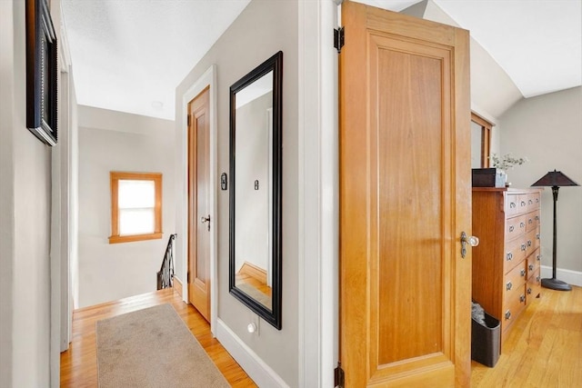 hallway with vaulted ceiling, light wood-type flooring, an upstairs landing, and baseboards