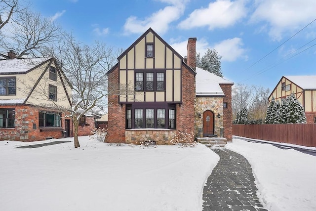 tudor house featuring stone siding, a chimney, fence, and stucco siding