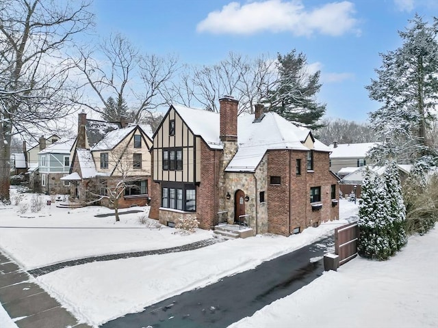 tudor house with a garage, brick siding, and a chimney