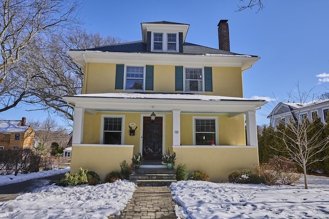 american foursquare style home with a chimney, a porch, and stucco siding