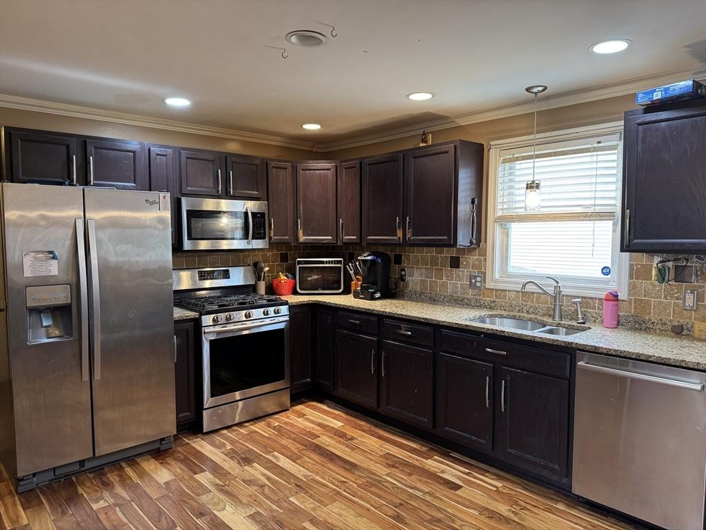 kitchen featuring crown molding, decorative backsplash, light stone countertops, a sink, and stainless steel appliances