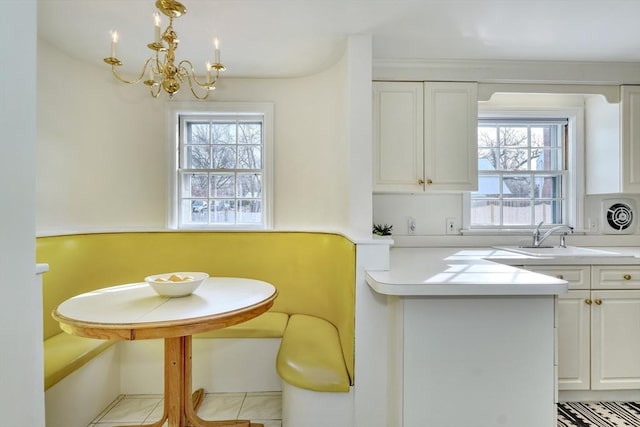 kitchen with light countertops, a peninsula, an inviting chandelier, white cabinets, and a sink