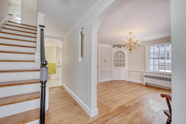 interior space with radiator, baseboards, stairs, light wood-style floors, and arched walkways