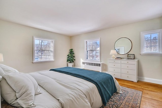 bedroom with baseboards, radiator, and light wood-style flooring