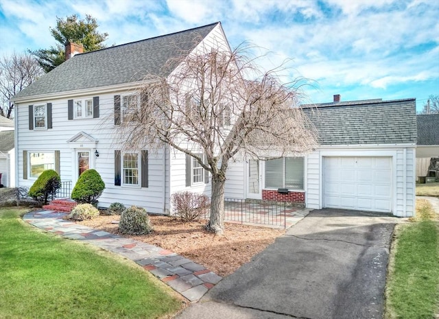 colonial home featuring a garage, a shingled roof, a chimney, and aphalt driveway