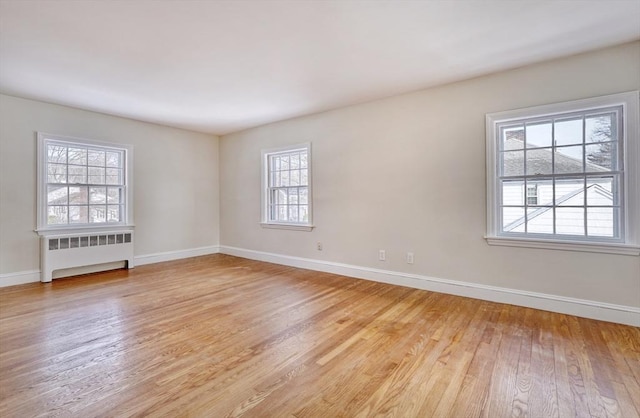 spare room with baseboards, radiator, and light wood finished floors