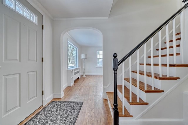 entryway with baseboards, arched walkways, stairs, light wood-style floors, and crown molding